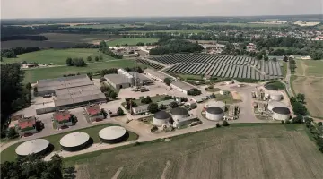 Luftansicht der Biogasanlage der DAH Gruppe im brandenburgischen Putlitz bei blauem Himmel. Drumherum grüne Felder.